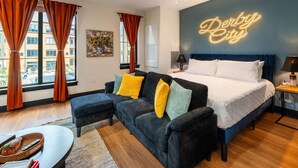 A modern hotel room with a bed, a sofa, a desk, and a neon sign.