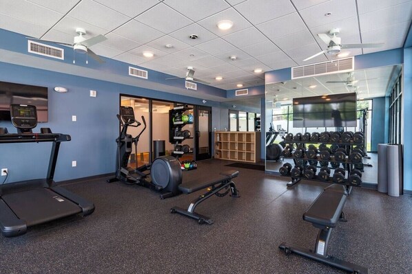 Une salle de sport équipée de tapis de course, d’un appareil elliptique, de poids libres et d’un miroir.