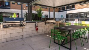 An outdoor patio with a grill, chairs, and a table.