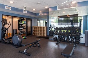 Un gimnasio con equipo de ejercicio, cinta de correr, mancuernas y una pantalla de televisión.