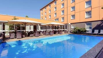 A hotel with a swimming pool, outdoor seating, and a multi-story building.