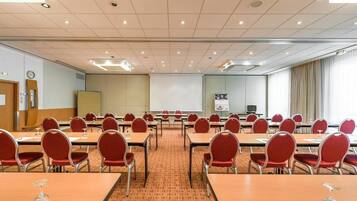 Uma sala de conferências com várias mesas e cadeiras, uma tela de projeção e um relógio na parede.