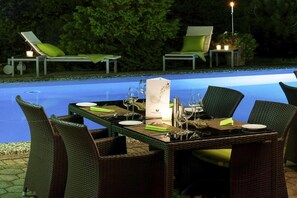 Ein Essbereich im Freien mit Korbstühlen und einem Tisch, gedeckt für eine Mahlzeit, neben einem Pool.