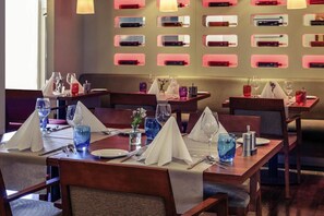 Ein Restaurant mit mehreren für den Genuss gedeckten Tischen, jede mit weißer Tischdecke, Besteck und blauem Glas.
