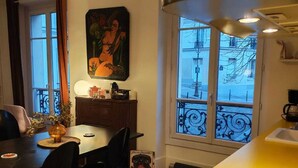 Un comedor con una mesa, sillas, un cuadro y una ventana con vistas a edificios.