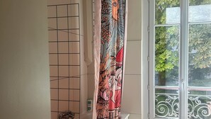 Un baño con bañera, ducha, ventana con vistas a follaje y una toalla en el suelo.