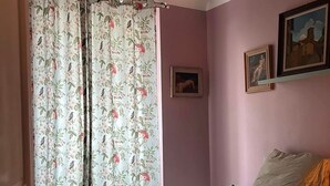 Un dormitorio con cama, cortinas florales, un cuadro enmarcado, una lámpara colgante y una puerta.