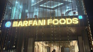 Un bâtiment avec une enseigne indiquant « Restaurant-Chambres-Farty Hall » et « Barfani Foods », doté d’une façade en verre, et des personnes à l’extérieur.