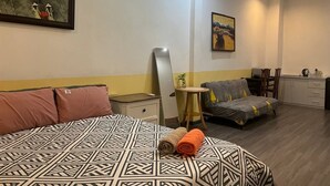 Quarto de hotel com cama, sofá, uma mesinha, espelho e um quadro na parede.
