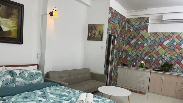 Um quarto com uma cama, um sofá, uma mesinha redonda pequena, uma cozinha compacta e uma parede com padrão.