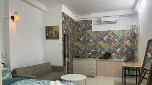 Um quarto com uma cama, um sofá, uma mesinha, uma cadeira, um quadro e uma parede com padrão colorido.