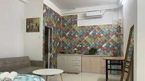 Um espaço de estar compacto com sofá, mesa de jantar redonda, área de cozinha compacta e parede estampada.