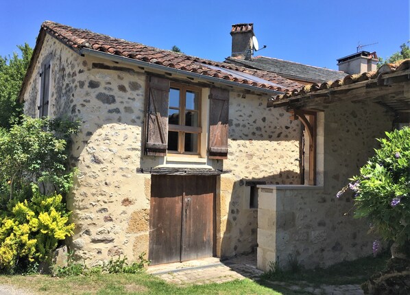 Ein rustikales Steinhaus mit Ziegeldach, Holztür und kleinem Fenster mit Fensterläden.