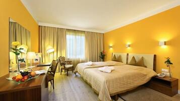 Habitación de hotel con una cama grande, un escritorio con lámpara, una silla y una mesita con fruta.