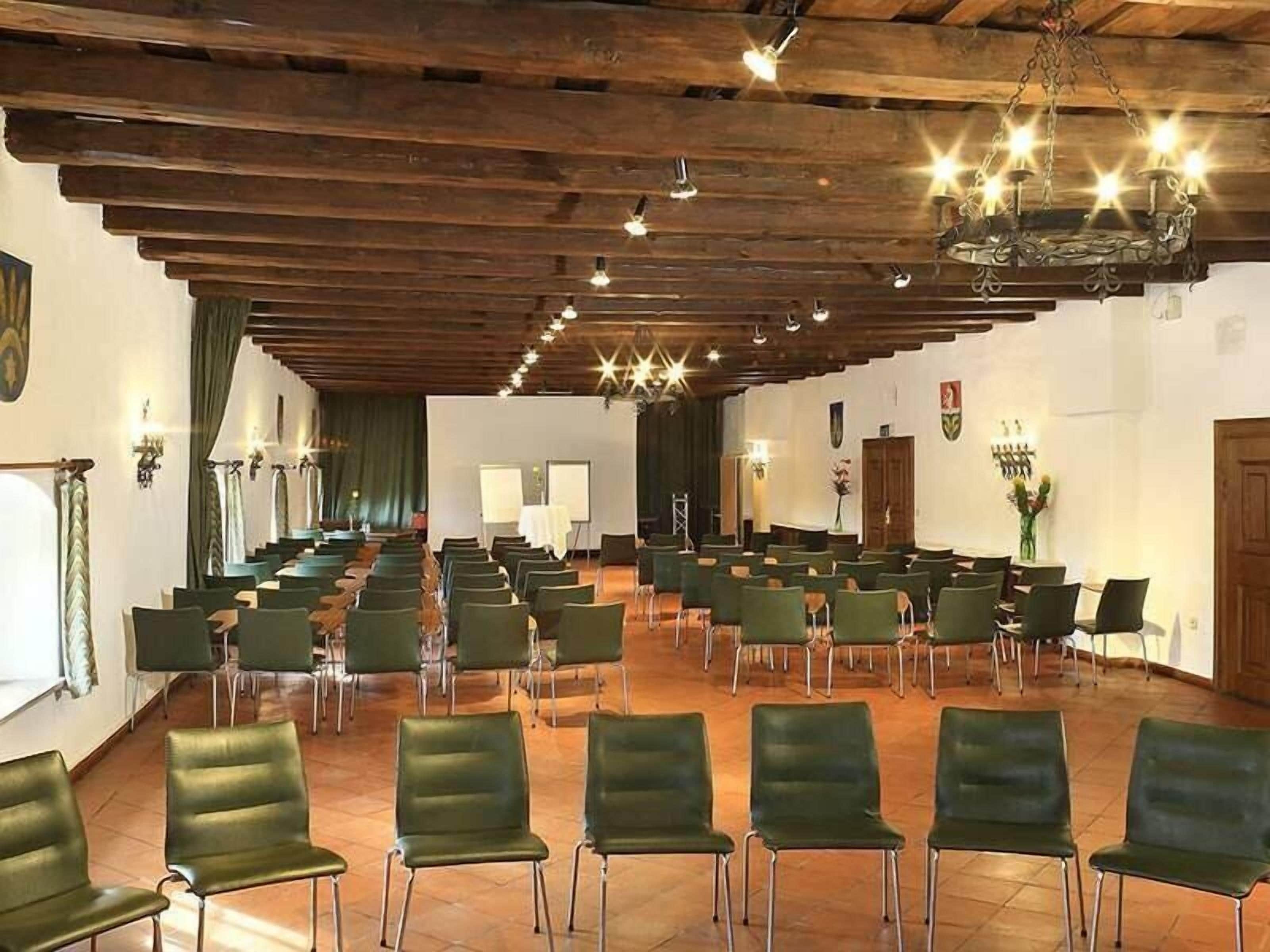 Ein Konferenzraum mit Stuhlreihen, Holzbalkendecke und Wandleuchten.