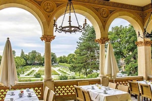 Uma área de refeições ao ar livre com mesas, cadeiras e vista para um jardim paisagístico.