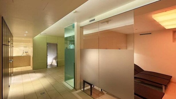 Pasillo moderno de hotel con separadores de vidrio, un banco y una zona de recepción.