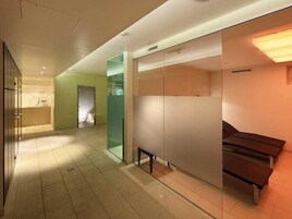 Pasillo moderno de hotel con separadores de vidrio, un banco y una zona de recepción.