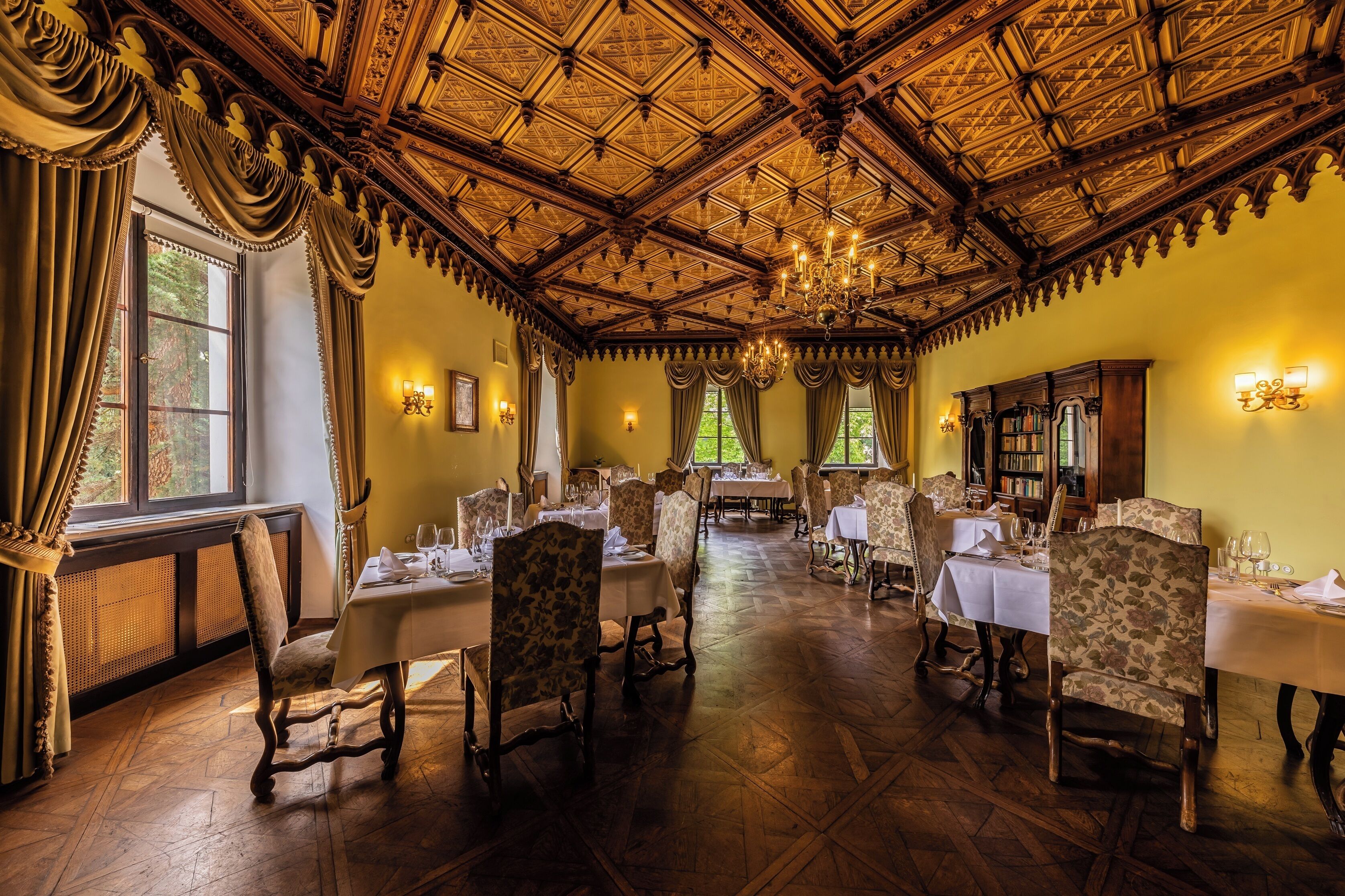 Comedor con techo de madera decorado, candelabros y muebles clásicos.