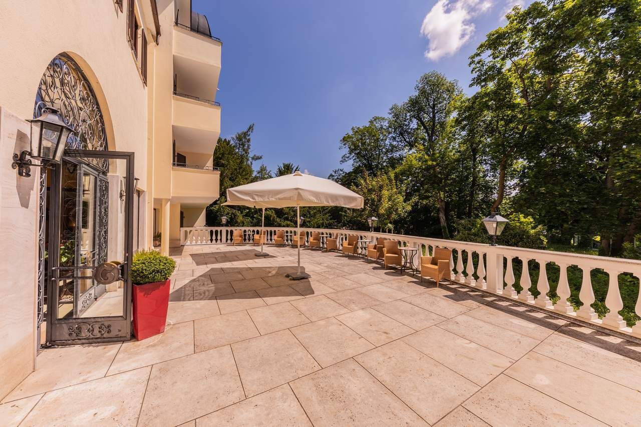 An outdoor patio with a white umbrella, seating, and a red planter.