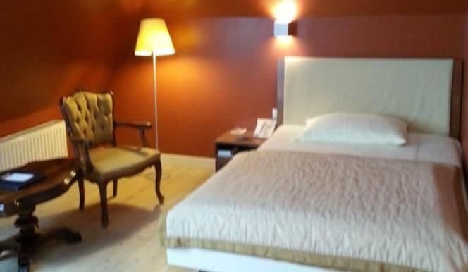 A hotel room with a bed, a chair, a nightstand, and a lamp.