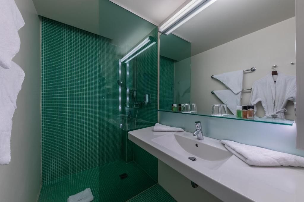 Un baño moderno con cabina de ducha de vidrio, un lavabo blanco y un espejo con repisa de vidrio arriba.