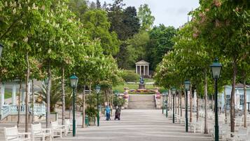 A park pathway with benches and lampposts, leading to a statue and steps.