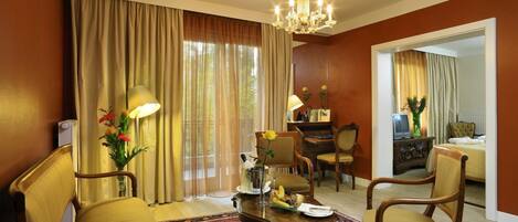Habitación de hotel con comedor, candelabro, ventana grande con cortinas y un espejo que refleja la habitación.
