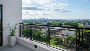 A balcony with a view of a city skyline, a potted plant, and a black metal railing. - Corporate Stays Zuba 8 -116 (Fernando de la Mora)