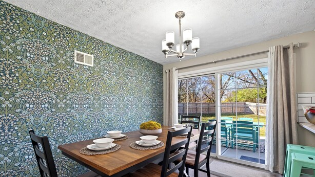 Un espace repas agrémenté d’un mur à motifs, d’un lustre et d’une vue sur l’extérieur grâce à une porte vitrée.