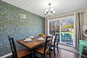 Un espace repas agrémenté d’un mur à motifs, d’un lustre et d’une vue sur l’extérieur grâce à une porte vitrée.