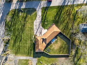 Vue aérienne d’une maison avec un toit en pente, une cour clôturée et un petit espace patio.