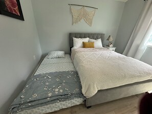 A bedroom with a bed, a nightstand, a macrame wall hanging, and a window with curtains. - Cozy retreat offering comfort and convenience to everything! (Anchorage)