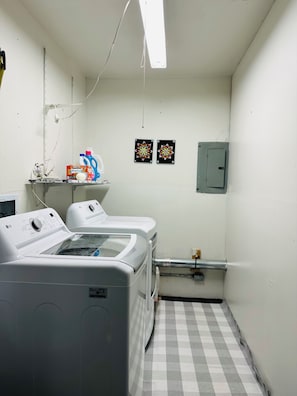 A laundry room with two front-loading LG washers, a shelf with laundry detergent, and two decorative wall hangings. - Cozy retreat offering comfort and convenience to everything! (Anchorage)