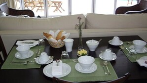 Une table à manger dressée pour le petit-déjeuner, avec de la vaisselle blanche, des couverts en argent et un vase rempli de fleurs.
