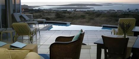 Una terraza con piscina, sillas de descanso, una mesa de comedor y vistas al mar.