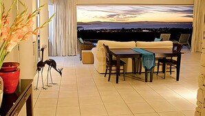 Un salon moderne avec un canapé, une table à manger, des chaises, une vue sur la ville au crépuscule et une sculpture décorative.