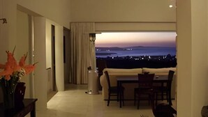 Un salon moderne avec vue sur la ville au crépuscule, un coin repas et un couloir menant à une autre pièce.