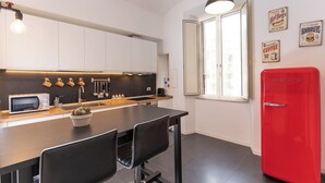 Een moderne keuken met witte kastjes, een rode koelkast, een eettafel met stoelen en een hangende lamp.