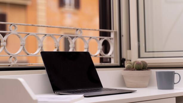 Een laptop op een witte tafel, een grijze mok en een pot met cactussen.