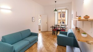 Een moderne woonkamer met een smaragdgroene bank, een houten eettafel en een groene hanglamp.