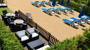 A rooftop pool area with lounge chairs and tables, surrounded by a wooden fence and greenery.