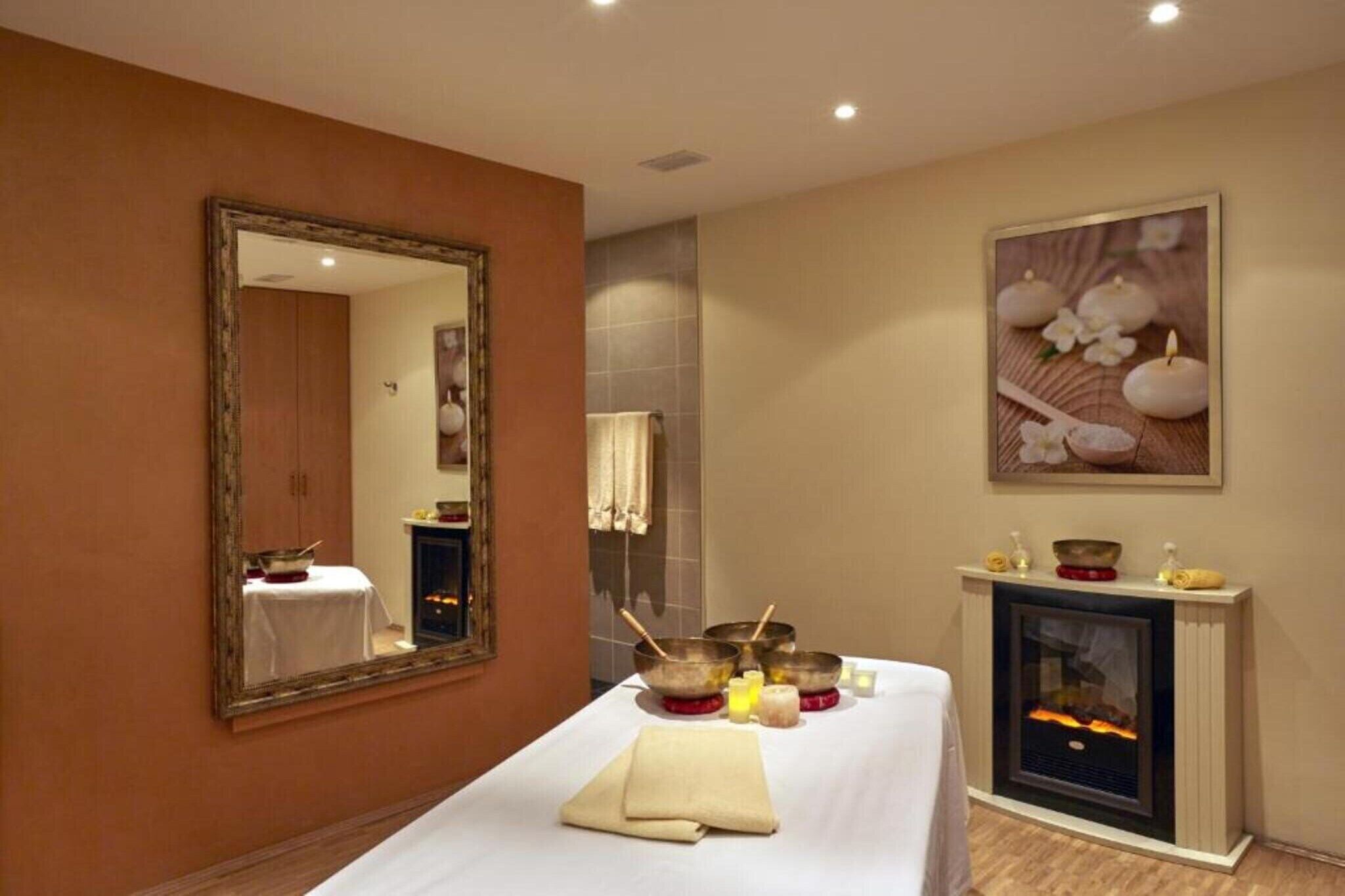 A room with a bed, a fireplace, a mirror, and a painting.