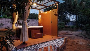 A covered outdoor seating area with a hot tub, wooden steps, and string lights.