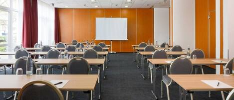 A conference room with multiple tables, chairs, a whiteboard, and a projector screen.