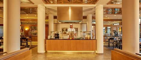 A hotel lobby with a central reception desk, high ceilings with a geometric pattern, and multiple seating areas.