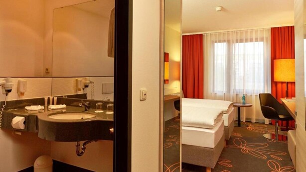 Ein Hotelzimmer mit Bad, Bett, Schreibtisch und Stuhl.