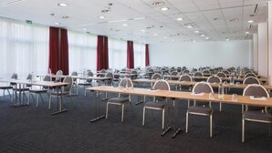 Ein Konferenzraum mit mehreren Tischen und Stühlen, großen Fenstern mit Vorhängen und einem Teppichboden.