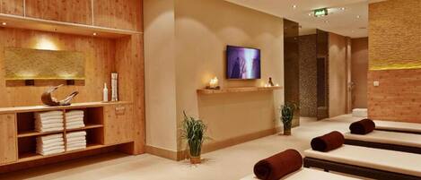 A spa room with wooden paneling, a television, and multiple massage tables.