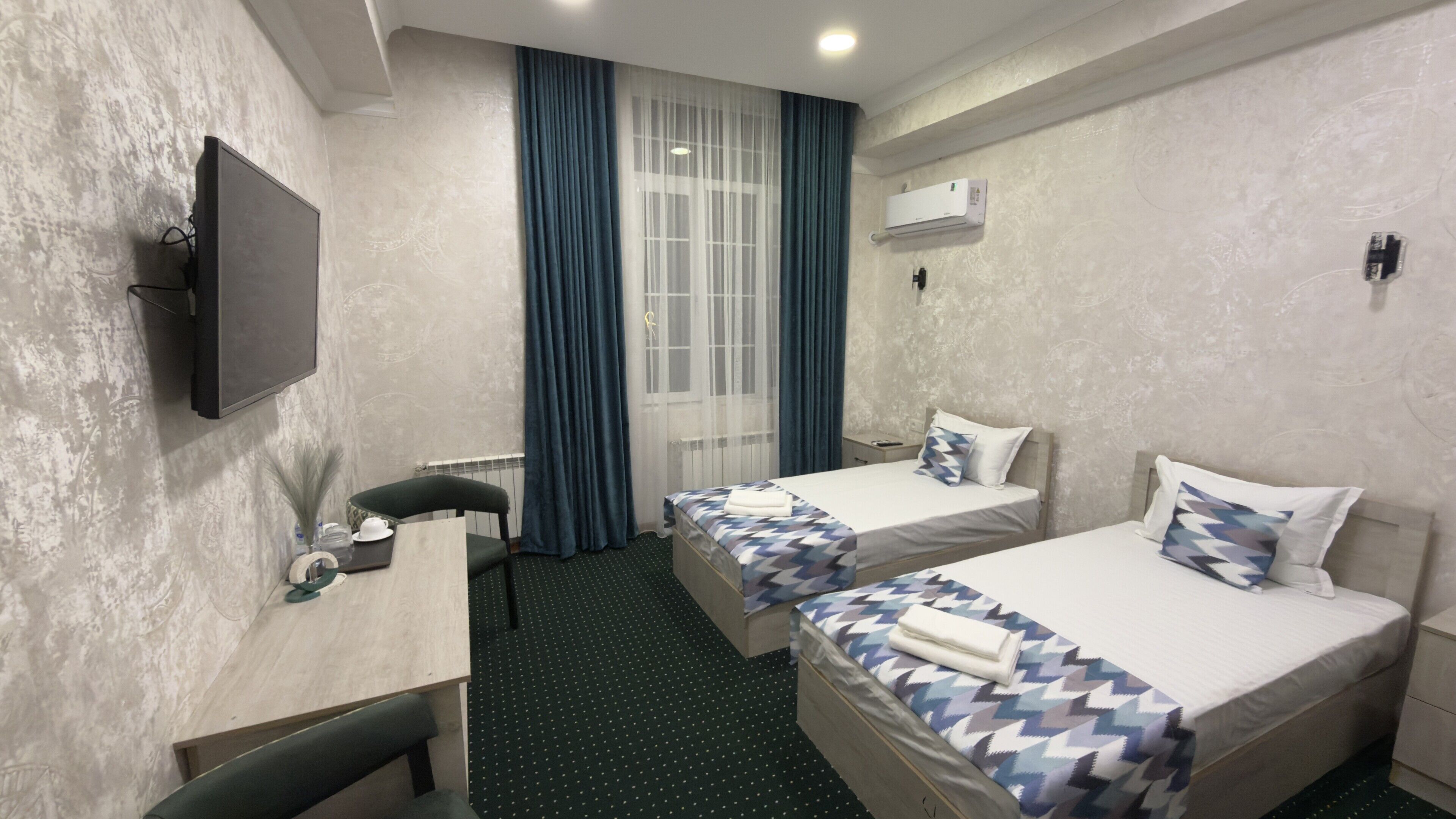 Ein Hotelzimmer mit zwei Betten, einem Schreibtisch, einem Sessel, einem Fernseher und einer Klimaanlage.
